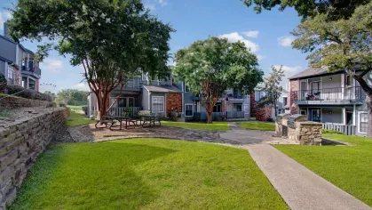 Outdoor picnic and grilling area with pathways, trees, and apartment buildings in the background