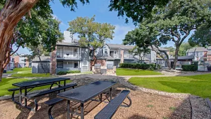 Shaded picnic area with metal tables and benches near apartment buildings and trees
