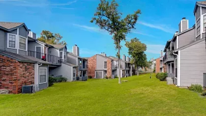 Open green space between apartment buildings with mature trees and balcony views