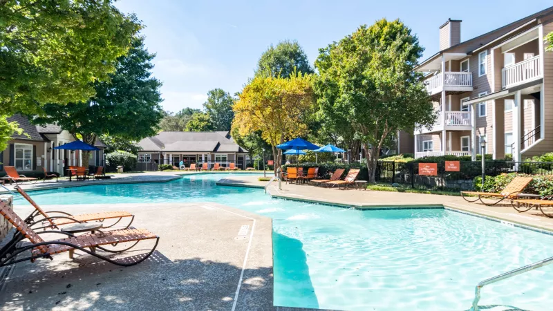 Resort-style swimming pool surrounded by orange lounge chairs and shaded seating under blue umbrellas.
