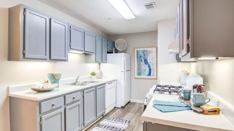 Galley-style kitchen with soft gray cabinets, white appliances, and wood-style flooring.