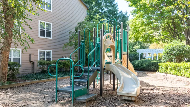 Outdoor playground with slides and climbing structures surrounded by trees and greenery.