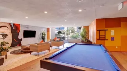 A stylish recreational room featuring a pool table, colorful artwork, and a spacious seating area with natural light.