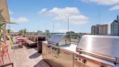 A rooftop grilling station with stainless steel barbecues, sleek countertops, and city views under a bright blue sky.