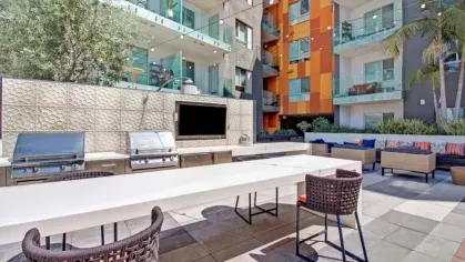 A well-lit outdoor gathering space with a built-in TV, barbecue area, and ample seating, perfect for entertaining.
