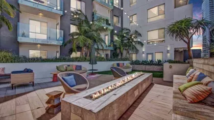 A cozy courtyard fire pit area surrounded by stylish seating, tropical plants, and string lights at dusk.