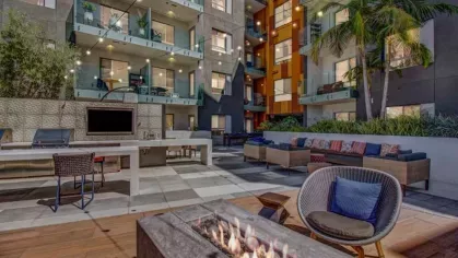 A courtyard with a long fire pit, contemporary outdoor furniture, and a grilling station, framed by modern apartment balconies.