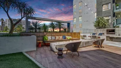 A sleek outdoor lounge area featuring a wooden bench with colorful cushions, a long fire pit, and ambient lighting against the cityscape.