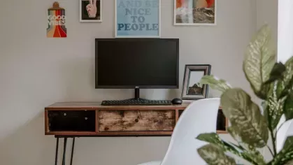 A work-from-home setup in the living area featuring a minimalist wooden desk, white chair, and a gallery wall for inspiration.