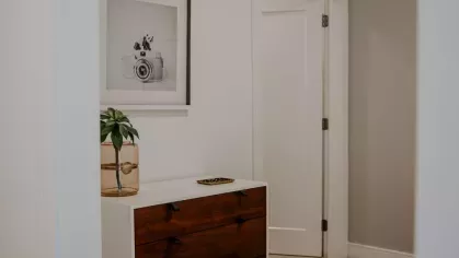 A stylish bedroom entryway at Industry Columbus Apartments featuring a modern wood and white dresser, a framed black-and-white camera print, and neutral-toned carpet.