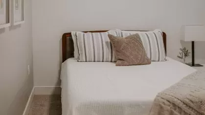 A modern bedroom with a sleek wooden bed frame, striped and textured pillows, and neutral décor for a warm and inviting atmosphere.