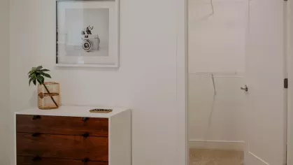 A spacious bedroom at Industry Columbus Apartments with a walk-in closet, a wooden dresser, and a framed art piece, blending functionality with elegant design.