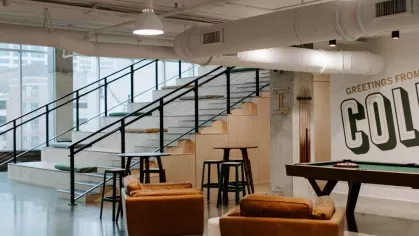 A modern lounge featuring leather chairs, a billiards table, and a "Greetings from Columbus" mural, offering a stylish and inviting communal space.