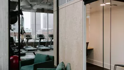 A dedicated work pod adjacent to the fitness center, featuring glass walls and modern seating for a productive work environment.