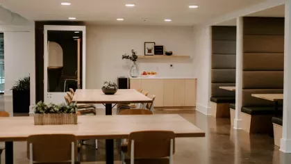A stylish lounge area at Industry Columbus Apartments featuring modern brown leather chairs, a pool table, and a staircase with built-in seating beneath an industrial-style ceiling.