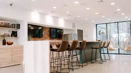 A spacious and well-lit community lounge in Industry Columbus Apartments, featuring high-top seating, hanging wicker chairs, and a kitchenette with modern finishes.