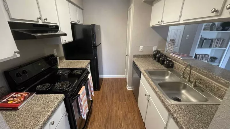 A spacious kitchen at The Oaks of Westchase Apartments featuring black appliances, sleek countertops, and ample cabinet storage.