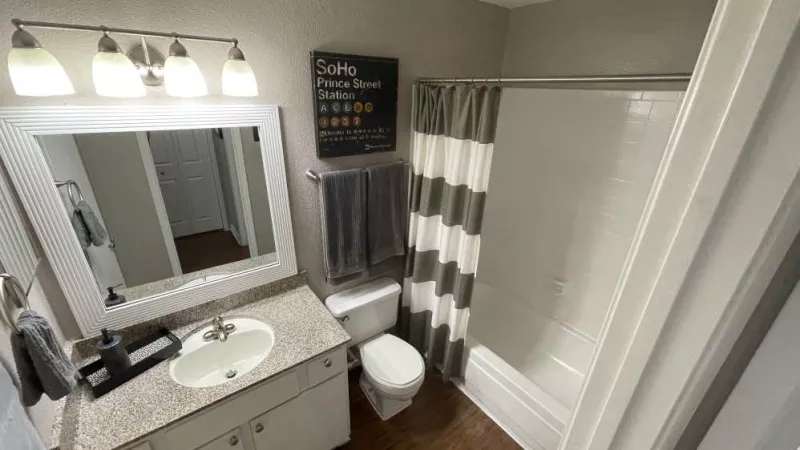 A sleek bathroom with a granite vanity, a well-lit mirror, modern lighting fixtures, and a shower-tub combination.