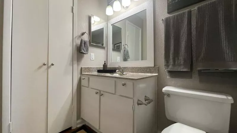 A stylish bathroom at The Oaks of Westchase Apartments featuring a framed mirror, dual lighting, a spacious vanity, and neatly folded towels for a polished look.
