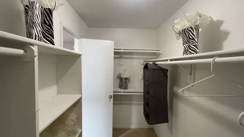 A well-organized walk-in closet with white shelving, hanging rods, and storage baskets, offering plenty of space for clothing and accessories.