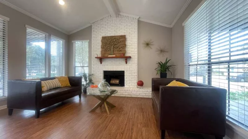 A bright and welcoming clubhouse seating area with a fireplace, tall windows, and contemporary décor at The Oaks of Westchase Apartments.
