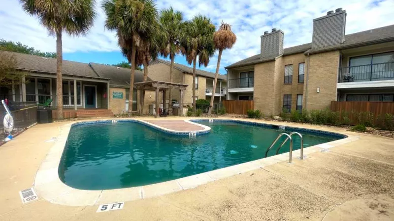 A sparkling outdoor pool surrounded by palm trees and apartment buildings, offering a refreshing retreat at The Oaks of Westchase.