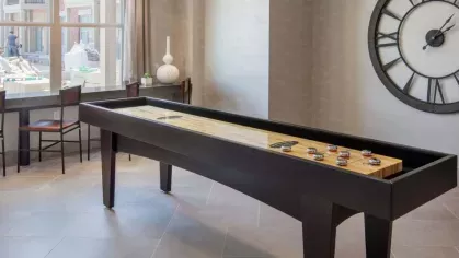 A modern game room featuring a shuffleboard table, large wall clock, and stylish pendant lighting.