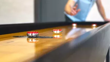 A resident enjoying a shuffleboard game in a stylish community space with warm lighting.