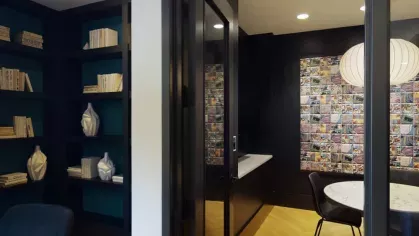 A contemporary private meeting room featuring dark walls, modern shelving, and a round table with seating.