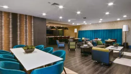  A vibrant co-working lounge with ample seating, bright teal walls, and floor-to-ceiling windows for natural light.