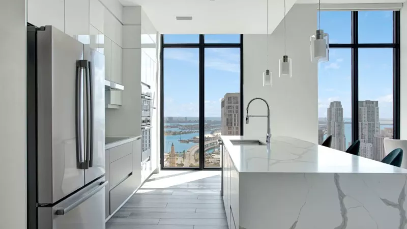 A contemporary kitchen with a marble island, stainless steel appliances, and panoramic city views.