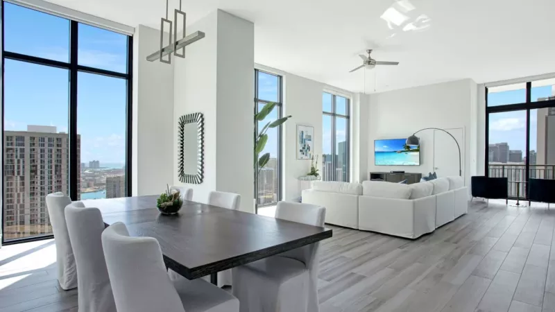 A spacious dining area with a dark wood table, white chairs, and expansive city views.