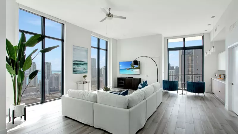 A bright living space with a white sectional sofa, large windows, and a cityscape view.