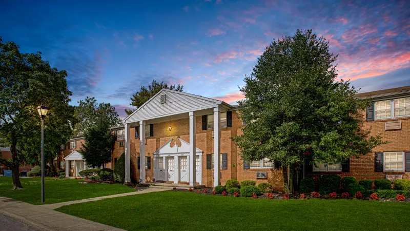 Charming exterior view of Miro Brickell Luxury Apartments at dusk, showcasing classic brick architecture, lush landscaping, and a beautifully lit entrance with a picturesque sunset sky.