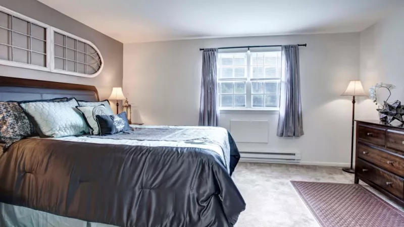 Spacious bedroom with a large bed, stylish bedding, soft carpeting, and natural light from a wide window at Silver Lake Manor Apartments.