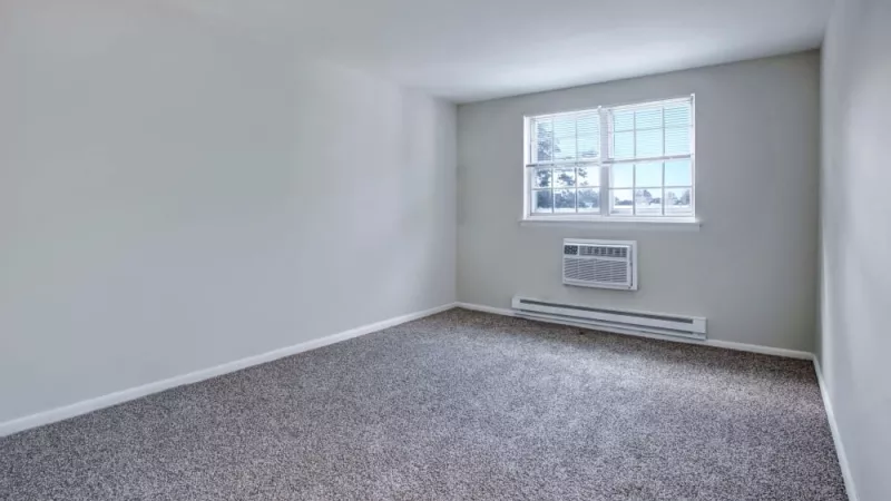 A bright and airy bedroom with a large window, plush carpeting, and a built-in air conditioning unit for year-round comfort.