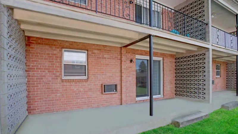 A private patio area outside a ground-floor apartment, showcasing brick walls, sliding glass doors, and decorative railings above.