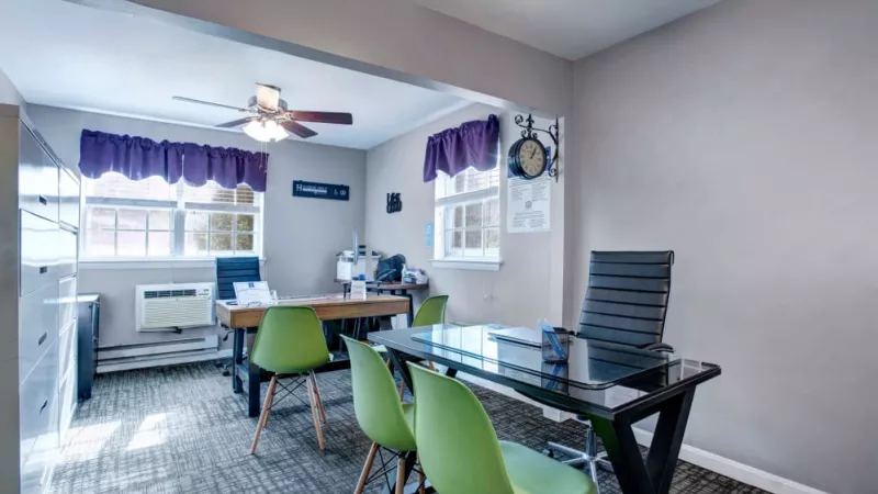 A cozy office space with a modern black desk, bright green chairs, and ample natural light, ideal for resident meetings and leasing inquiries.