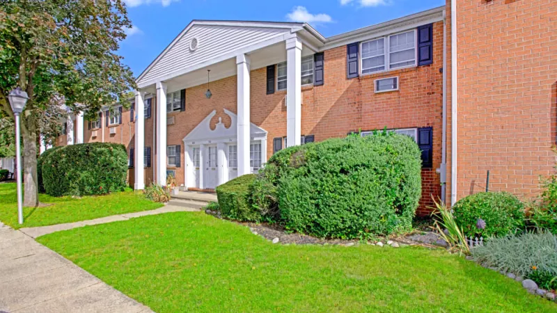 Exterior view of Silver Lake Manor Apartments showcasing a classic red brick facade, white columns, and lush green landscaping under a bright blue sky.