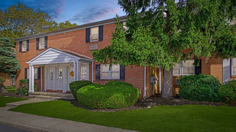 A tree-lined sidewalk leading to a well-maintained apartment building at Silver Lake Manor, with neatly trimmed hedges and a classic architectural design.