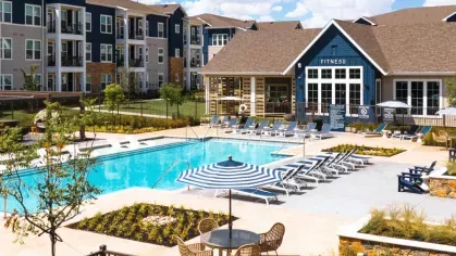 An aerial view of a resort-style pool surrounded by lounge chairs, umbrellas, and lush landscaping.