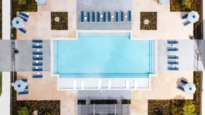 A resort-inspired pool deck with shaded seating, striped umbrellas, and a clubhouse with fitness amenities.