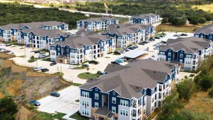 Expansive aerial view of a modern apartment community nestled in a scenic landscape, showcasing multiple three-story buildings and ample parking.
