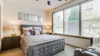A stylish bedroom featuring a deep gray upholstered bed, matching furniture, and expansive windows that bring in natural light, offering a warm and welcoming feel.