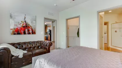 A spacious bedroom featuring a plush bed, a stylish leather couch, and an open doorway leading to a well-lit en-suite bathroom.