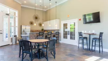 A bright and inviting resident lounge featuring high ceilings, stylish pendant lighting, and a kitchenette area, perfect for social gatherings.
