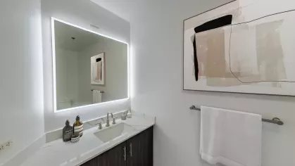 Elegant bathroom in Nari Koreatown penthouse featuring backlit mirror, abstract wall art, and white quartz vanity