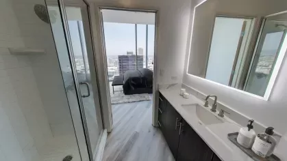 Luxurious penthouse bathroom at Nari Koreatown with glass shower, double-sink vanity, and bedroom view through open doorway