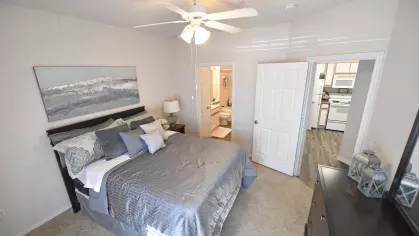 View of the primary bedroom with private en-suite bathroom and hallway access to the kitchen at Gates at Citiplace apartments.