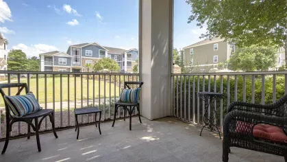 Covered balcony with black patio furniture, colorful accent pillows, and views of the landscaped courtyard.